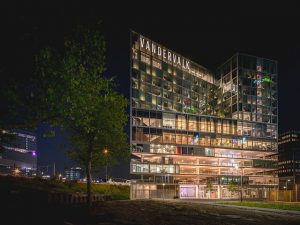 Foto van het exterieur van het Van der Valk Zuidas-hotel. Het is donker en het hotel is verlicht.